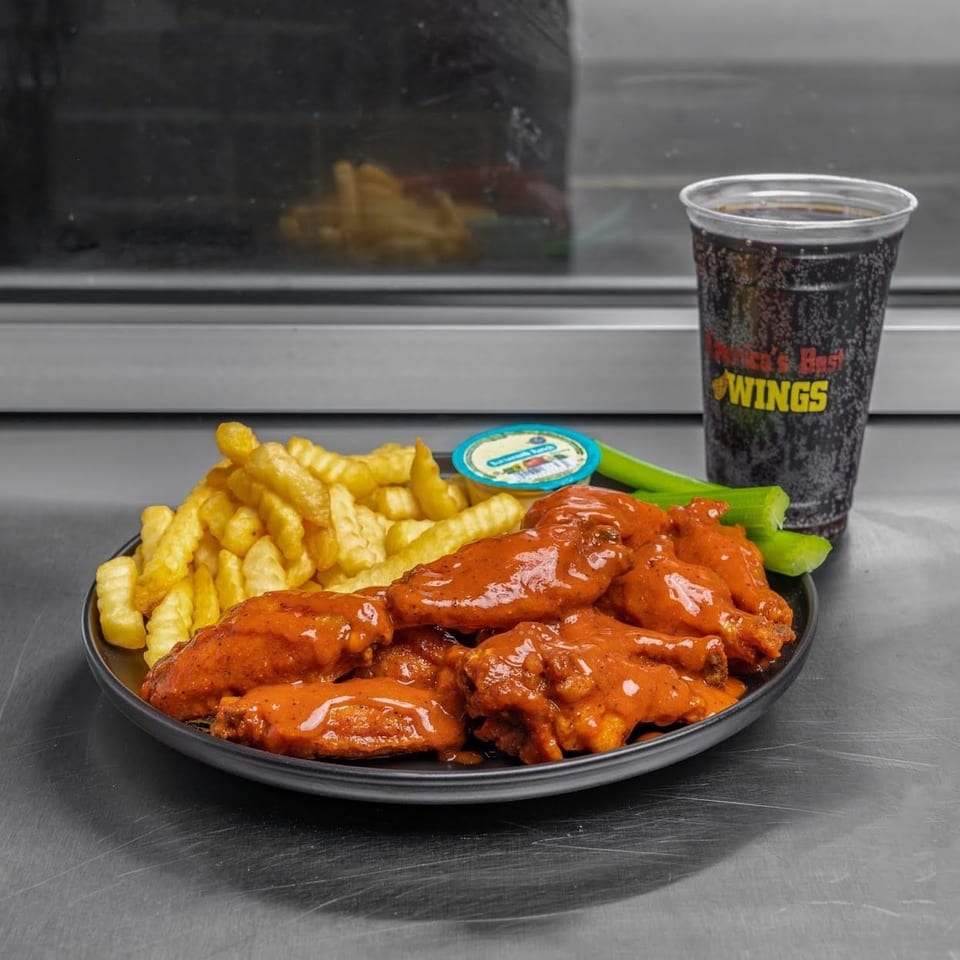 A plate of buffalo wings, crinkle-cut fries, celery sticks, ranch dip, and a soda.