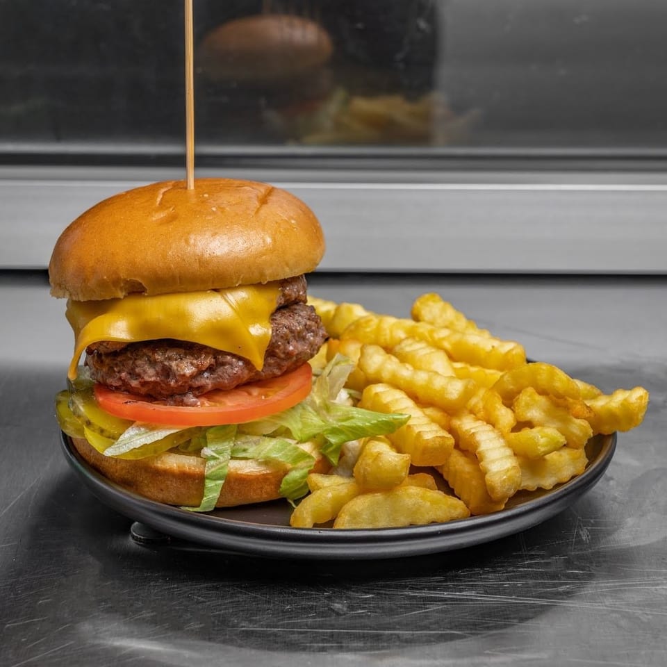 A cheeseburger with lettuce, tomato, and pickles, served with crinkle-cut fries on a black plate.
